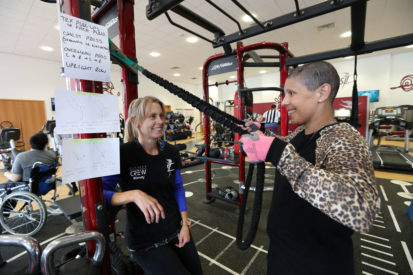 Gym instructor Wendy supporting lady using weights machine in gym