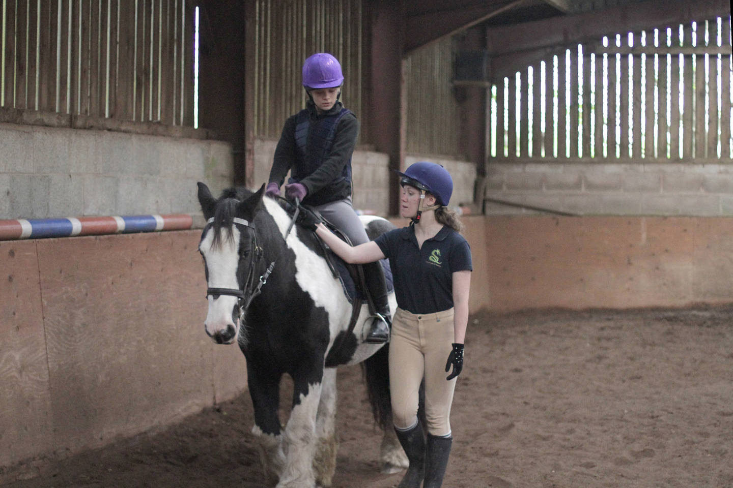 Young woman riding horse with support from trainer