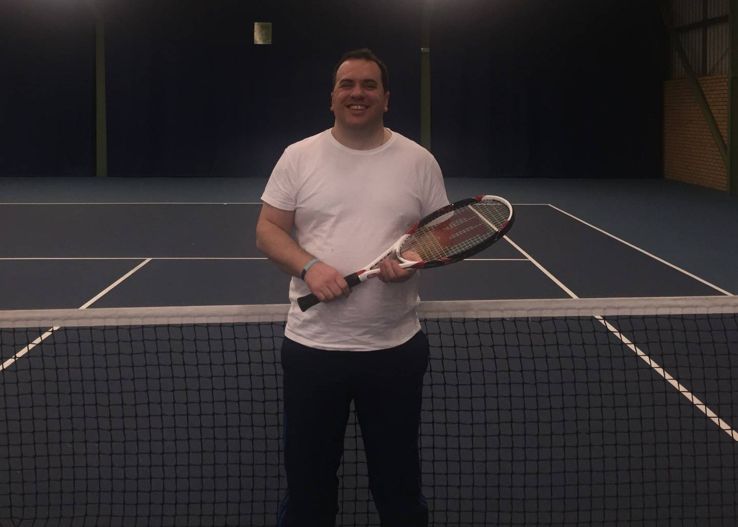 Matt standing by tennis net smiling to camera