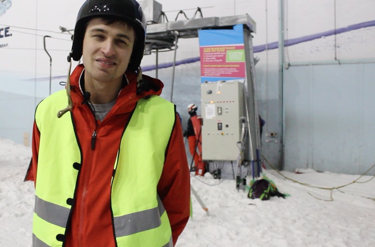 Josh smiling to camera with his skiing gear on at the bottom of the slopes at Manchester's Chill Factore. 