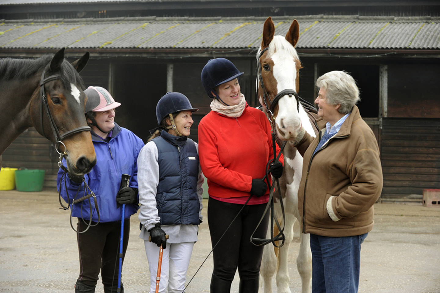 Group of disabled riders in paddock with two horses