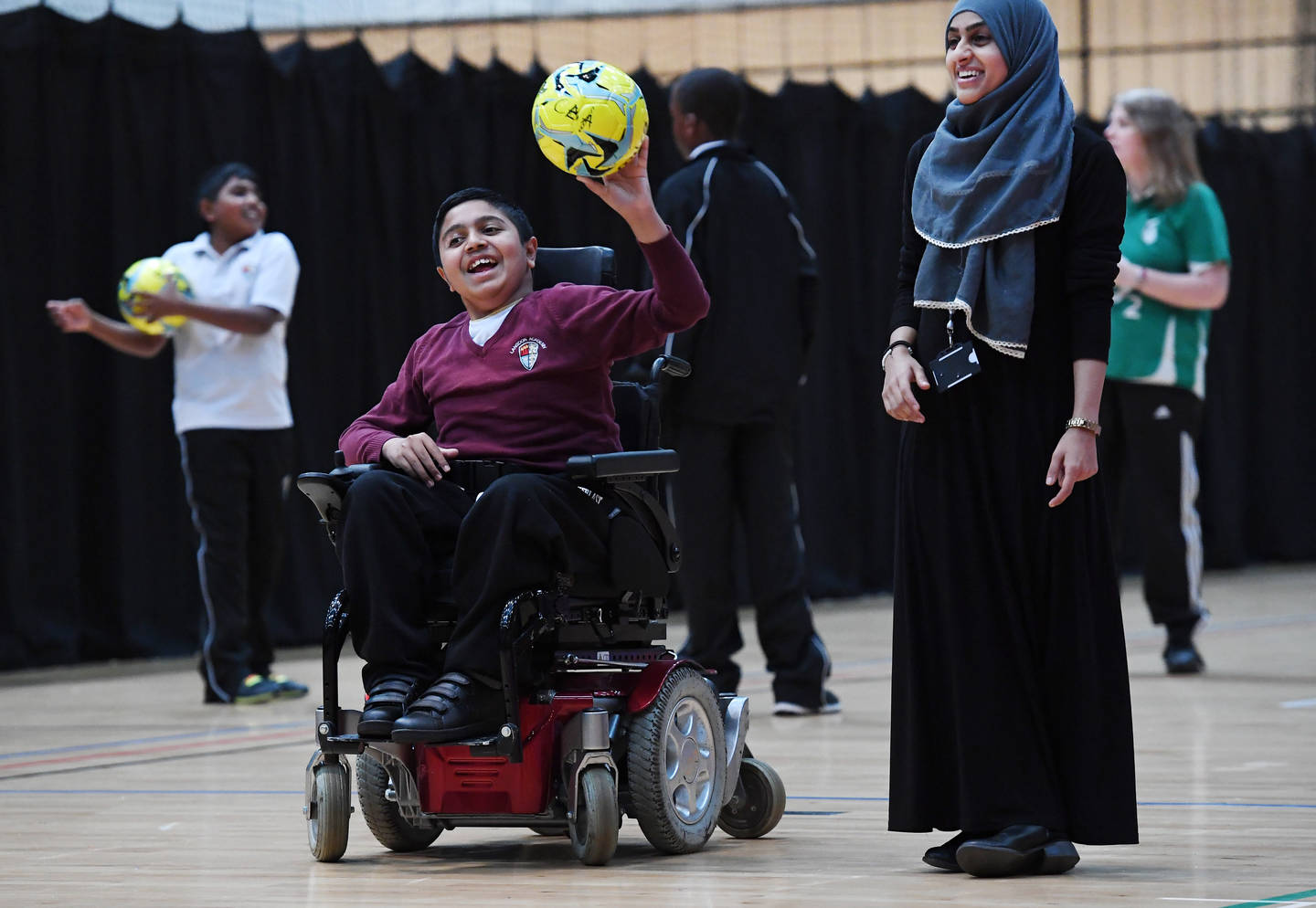Young boy in powerchair throwing football at school sports festival 