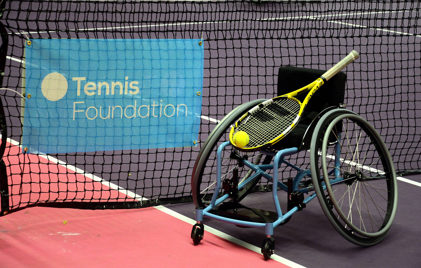 Tennis foundation logo on Tennis net, with a tennis racket and ball placed on a sports wheelchair. 