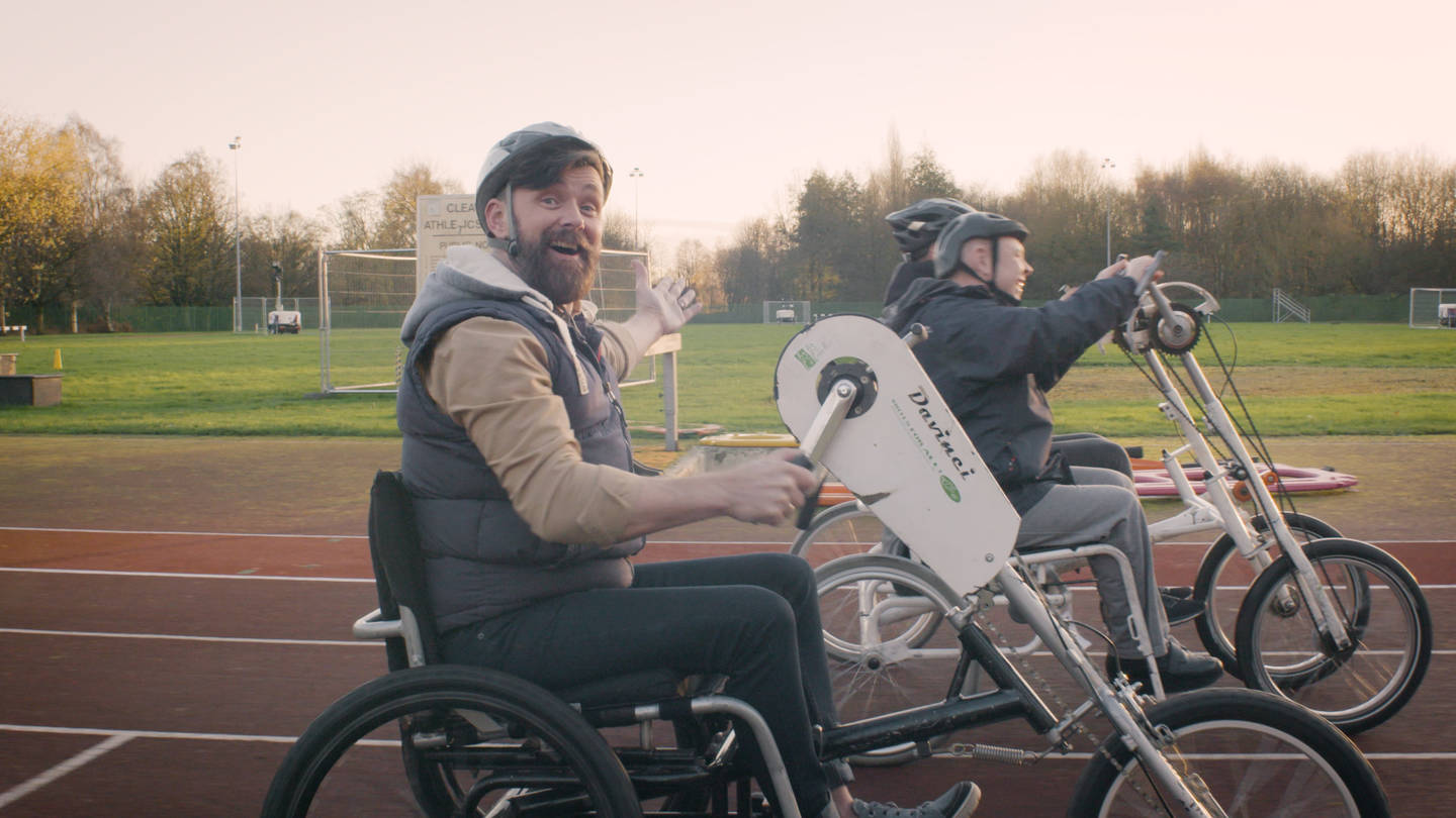 Presenter Kris and friends cycling on athletics track using an adapted bikes 