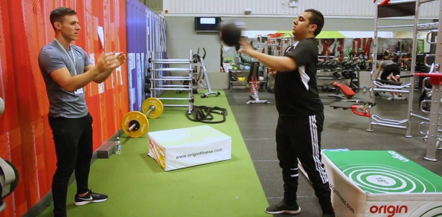 Sami training with Ben in the gym, throwing a medicine ball. 