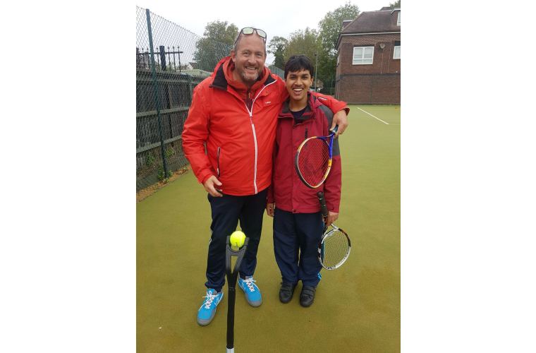 Neal with tennis coach smiling to camera with tennis rackets in hand. 