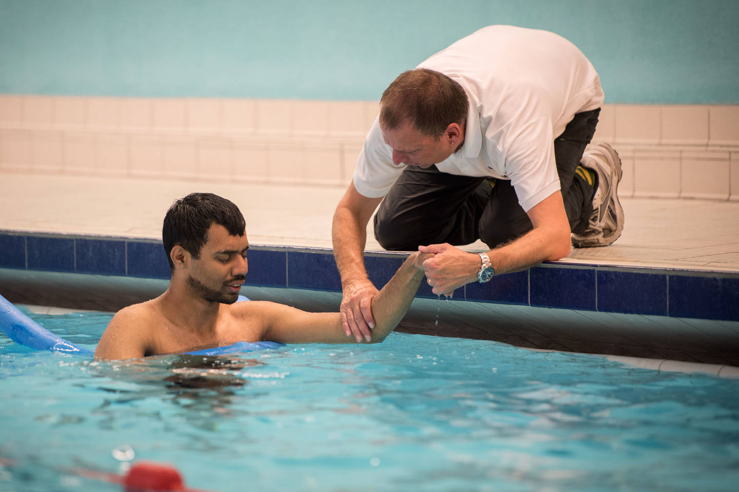 Swimming teacher supporting visually impaired man in swimming pool