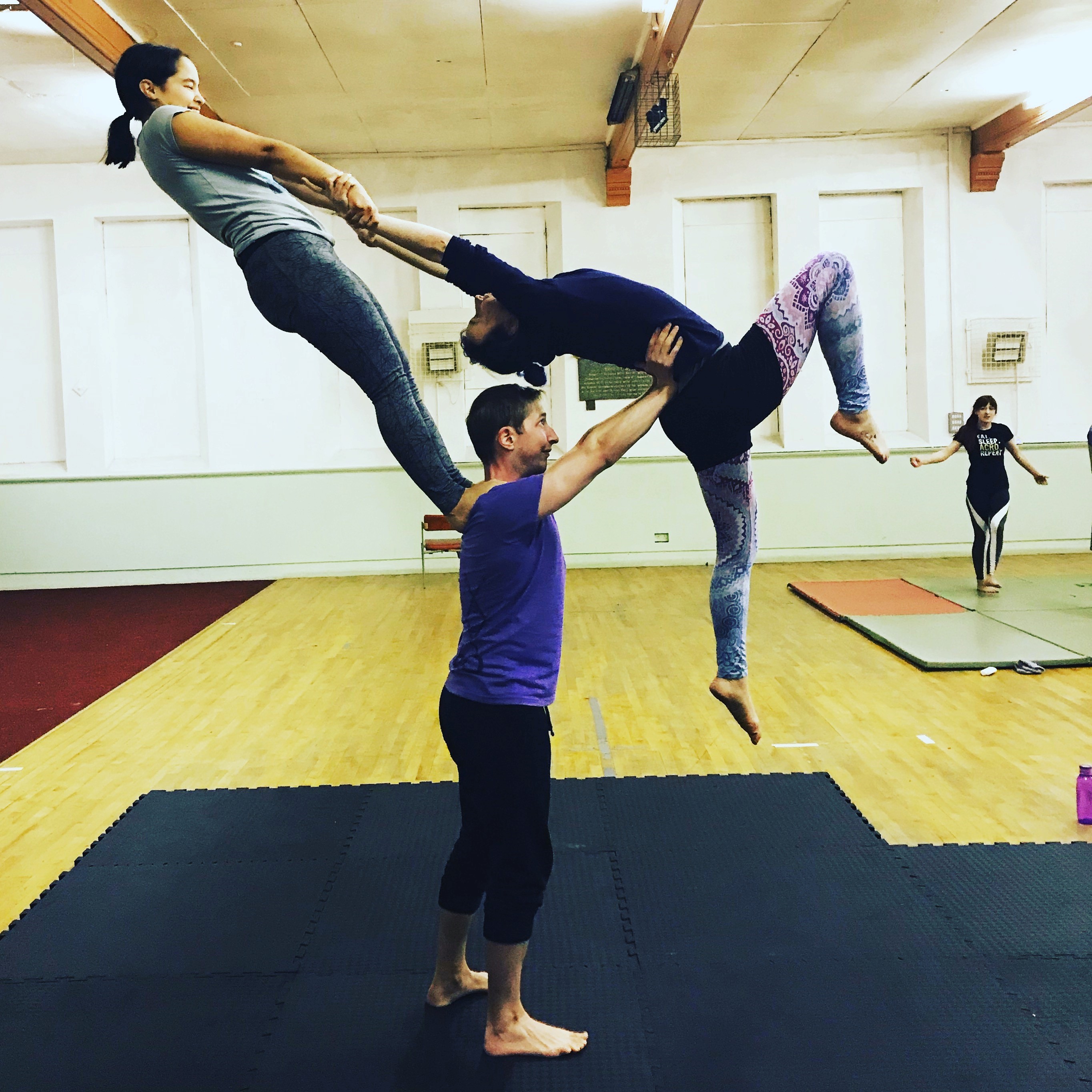 Ellie doing an acro balance move being held up by two other members. 