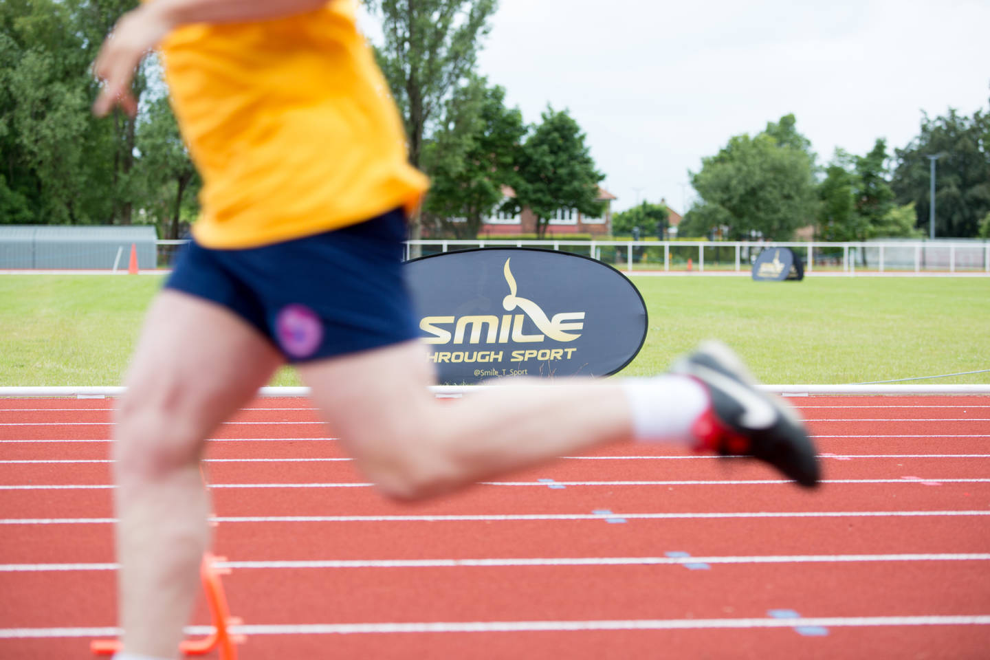 Person running on running track with Smile Through Sport logo in the background. 