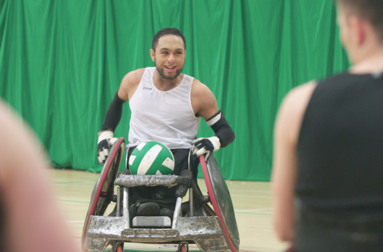 Wheelchair rugby player with ball smiling on court