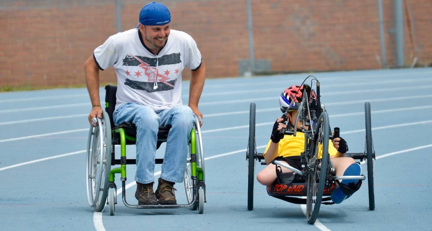 David Williamson with a child in an adapted bike going around a track.