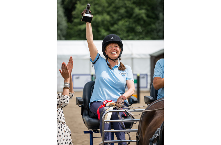 Disabled carriage rider holding trophy up in air. 