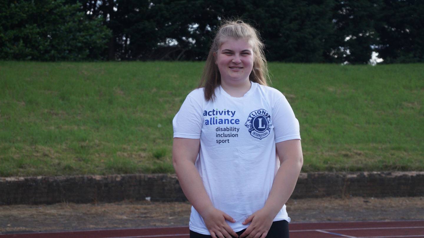 Ellie wearing Activity Alliance t-shirt on running track. 