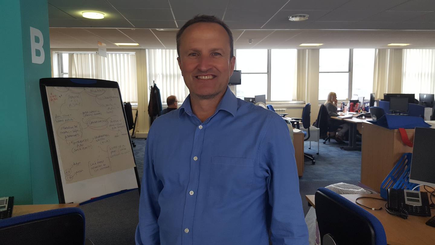 Simon smiling to camera in his offices. 