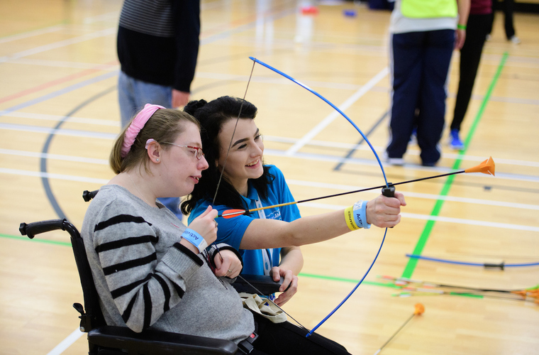Young woman in a wheelchair taking part in archery with supporter