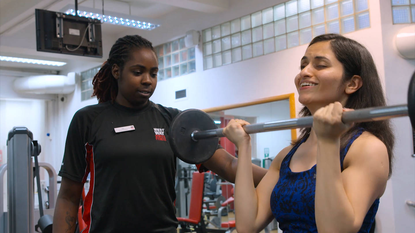Visually impaired woman working out in gym with support of her gym instructor. 