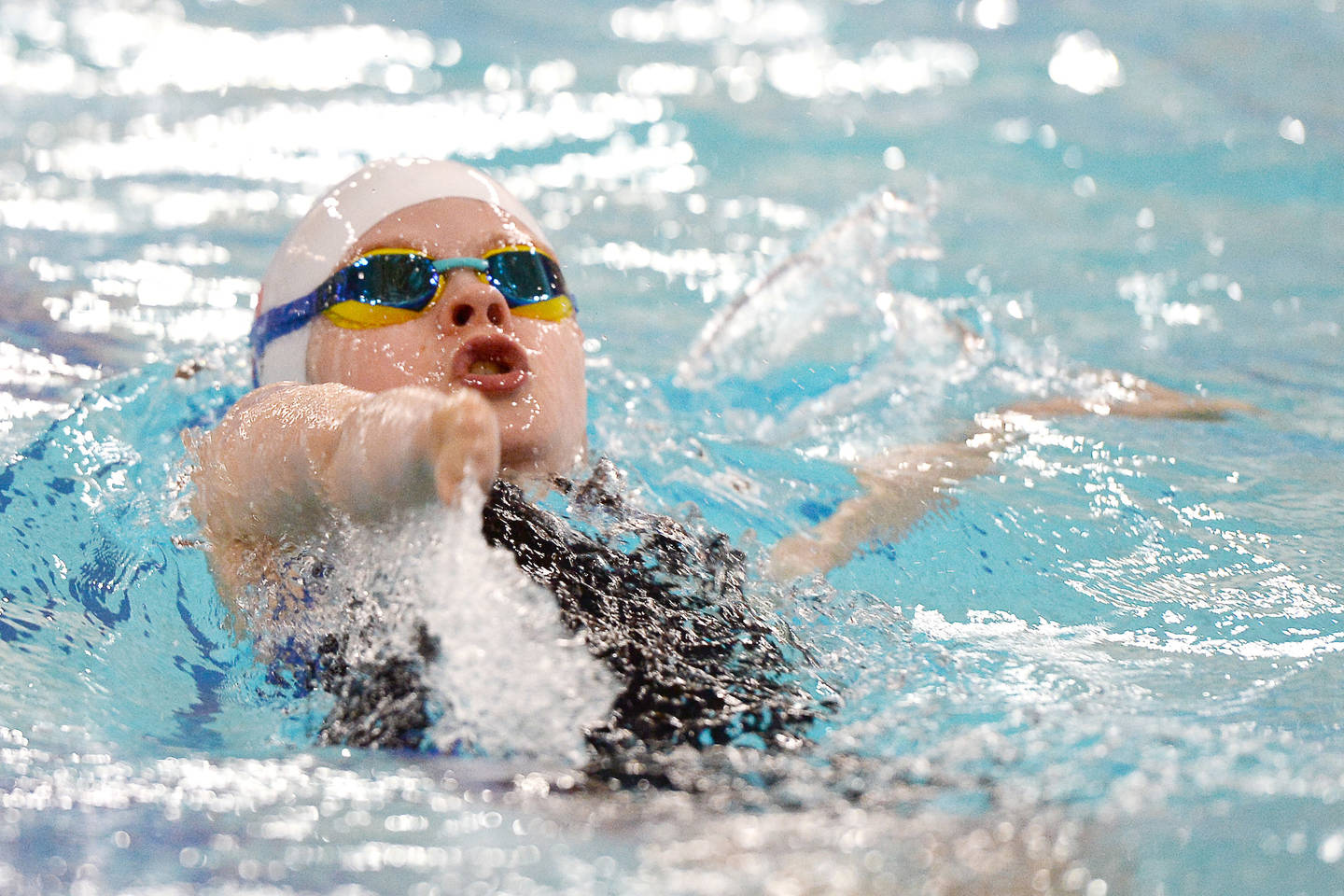 Young swimmer with upper limb impairment swimming backstroke in pool  