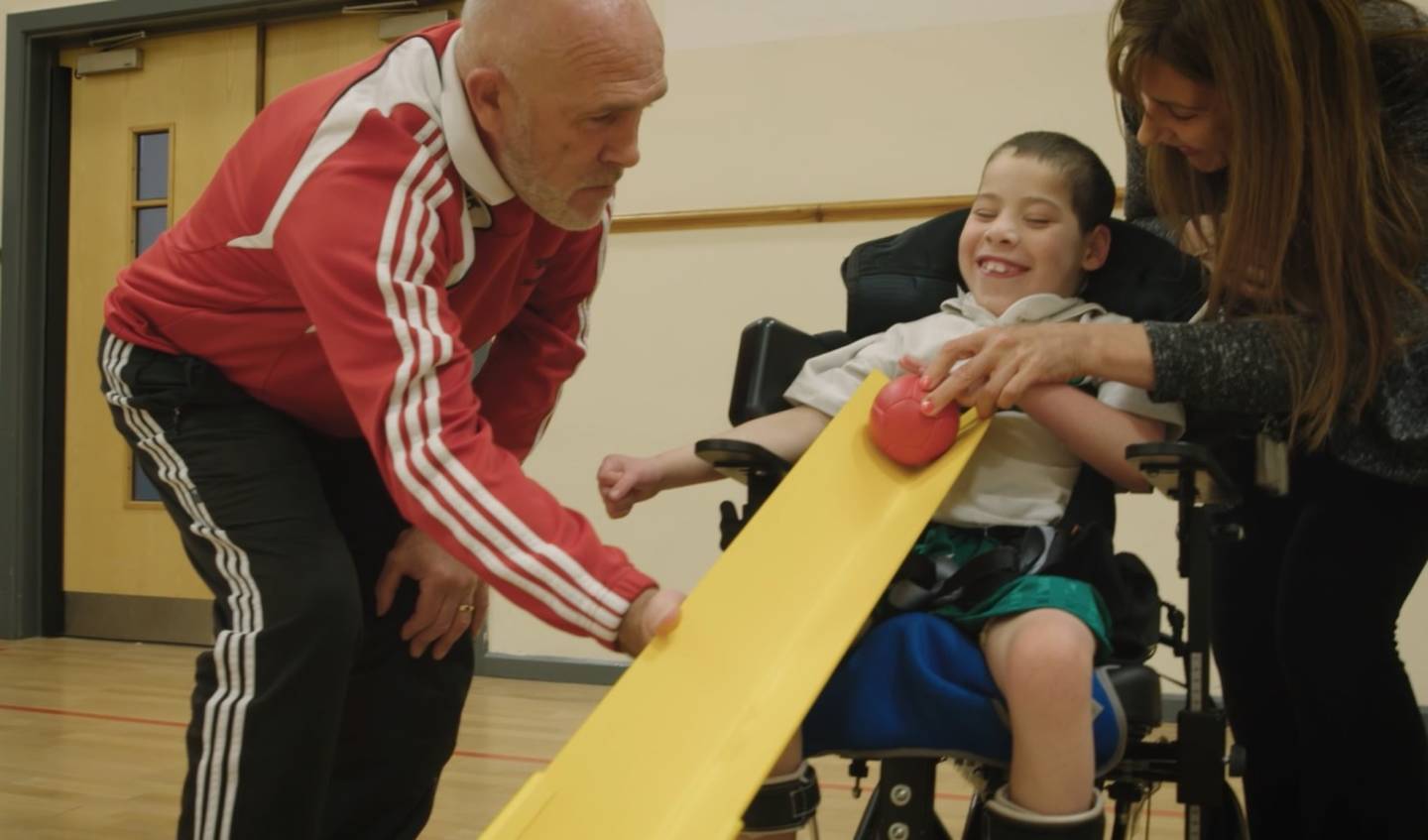 Young boy playing boccia with teacher and supporter 