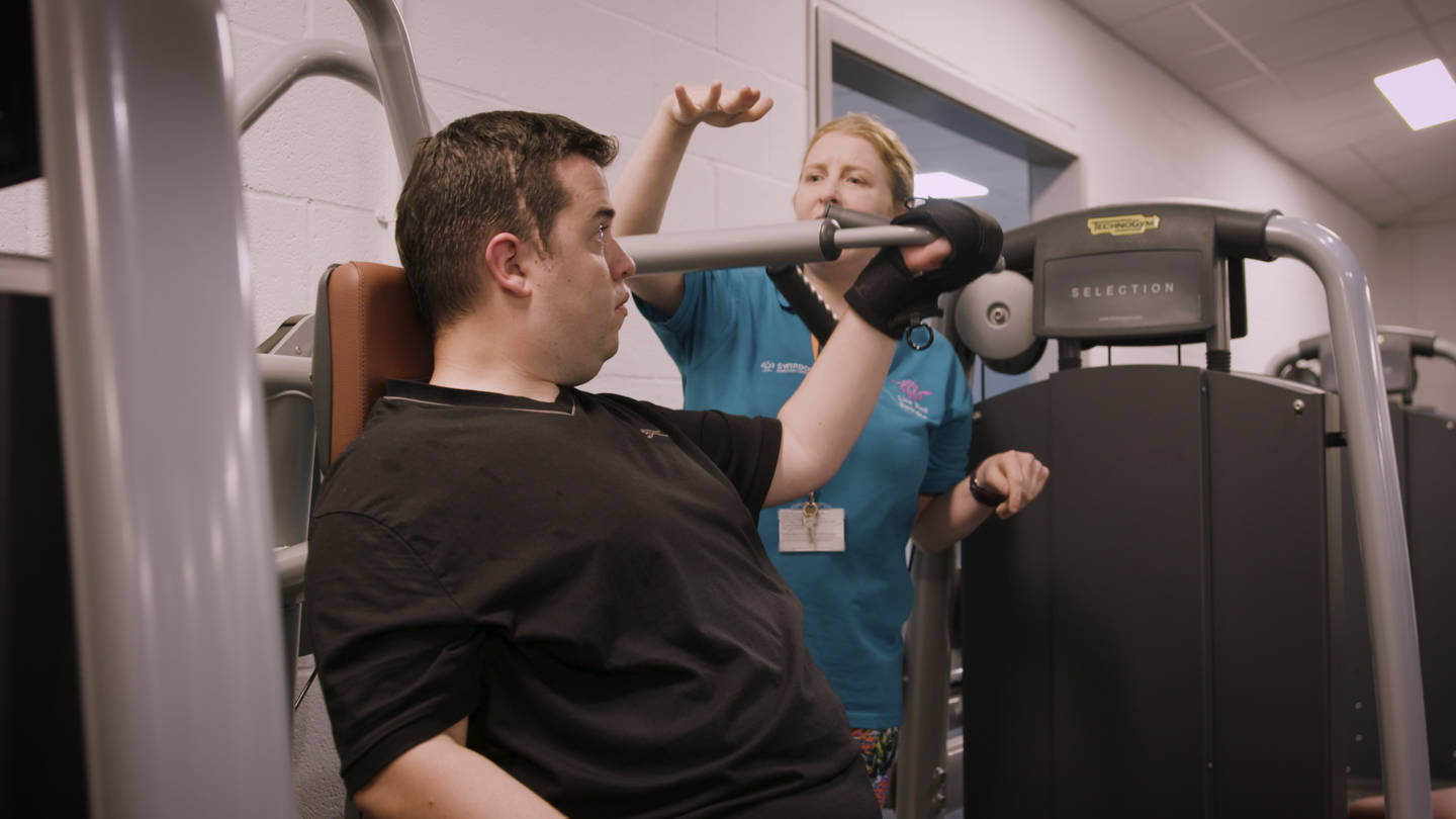 Persion instructing supporting disabled man in a gym