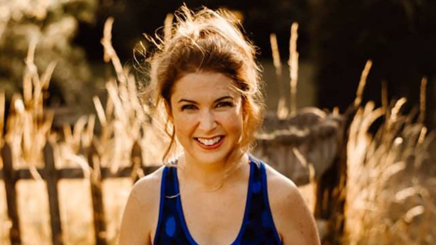 Miranda McCarthy smiling to camera with wooden fence and grass behind her. 