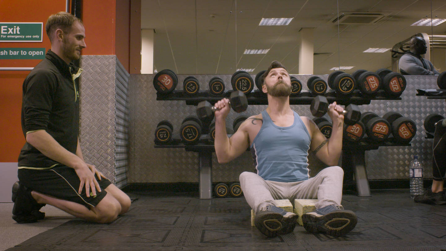 Disabled man using free weights in a gym with support from a personal trainer