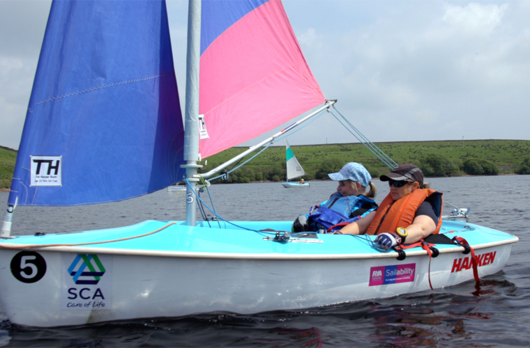Disabled woman sailing dinghy boat on a lake during an inclusive sailing session