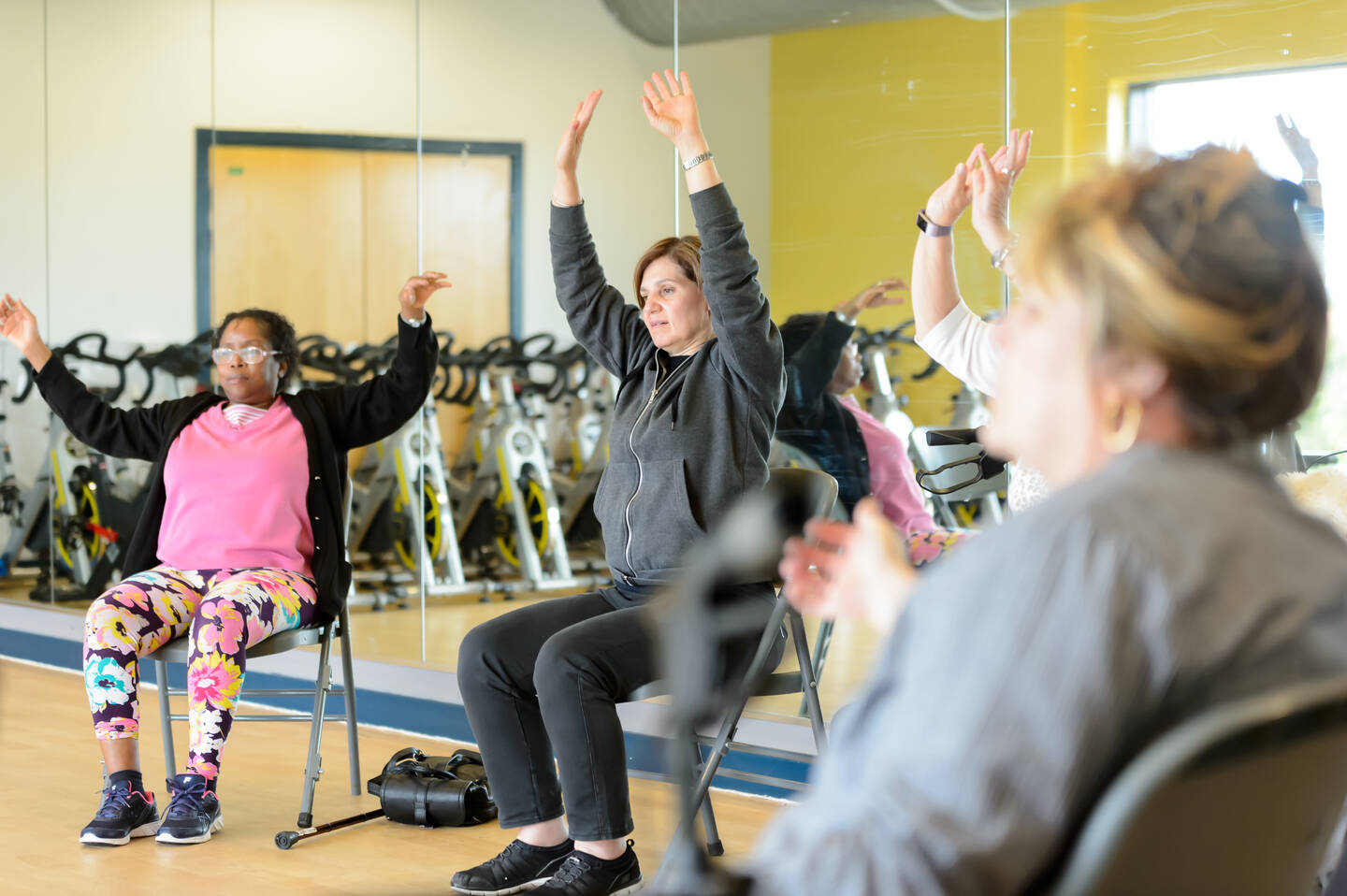 Two women raising their arms up in a seated yoga class 