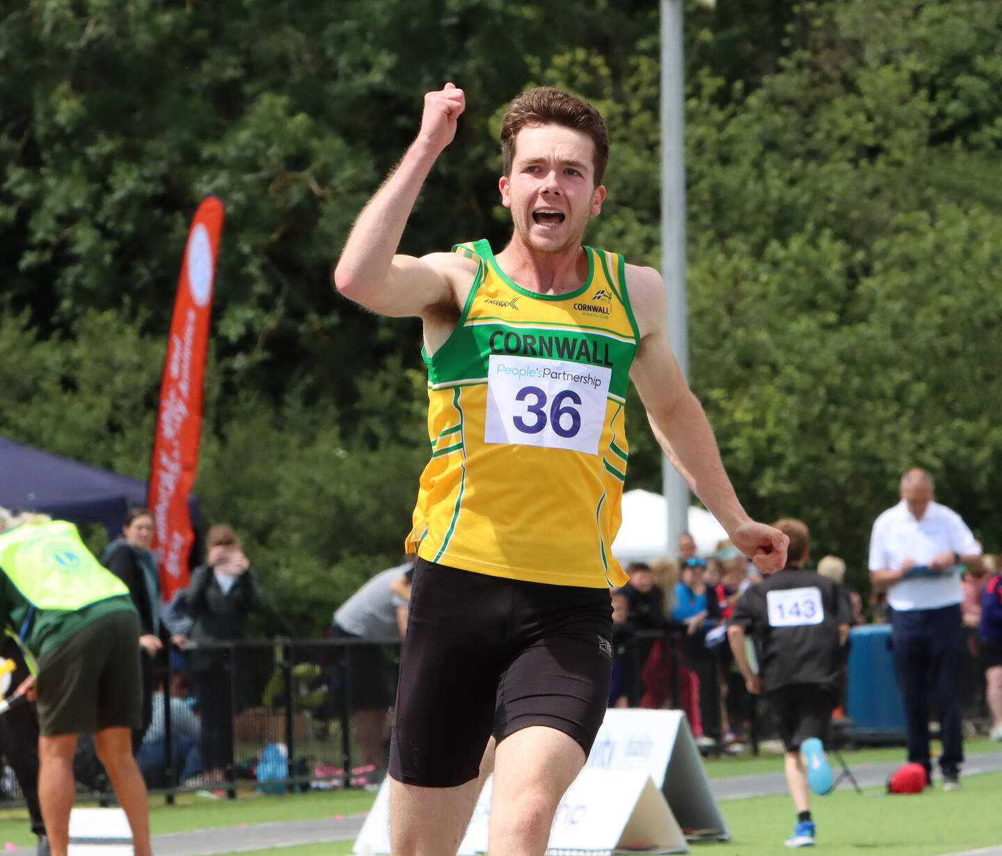 A sprinter in a yellow and green vest celebrates as they run.