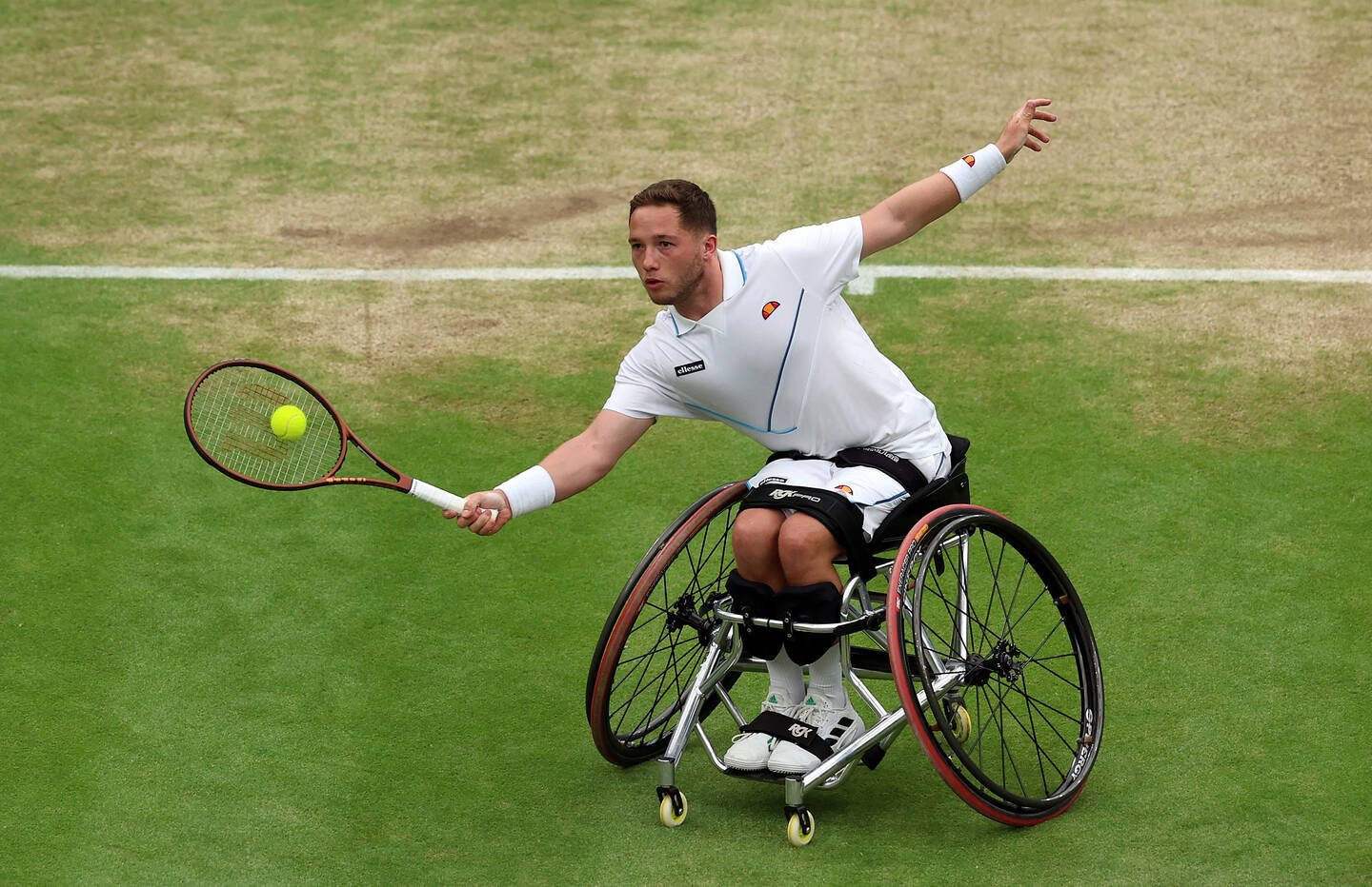 Alfie reaching for a shot in his wheelchair tennis chair on a grass court