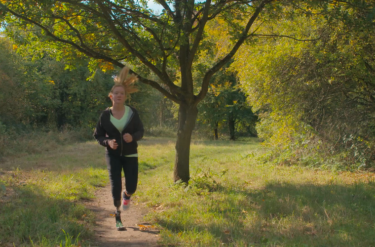 Cassie running in a park with her running blade on