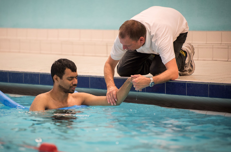 Swimming teacher supporting visually impaired man in swimming pool