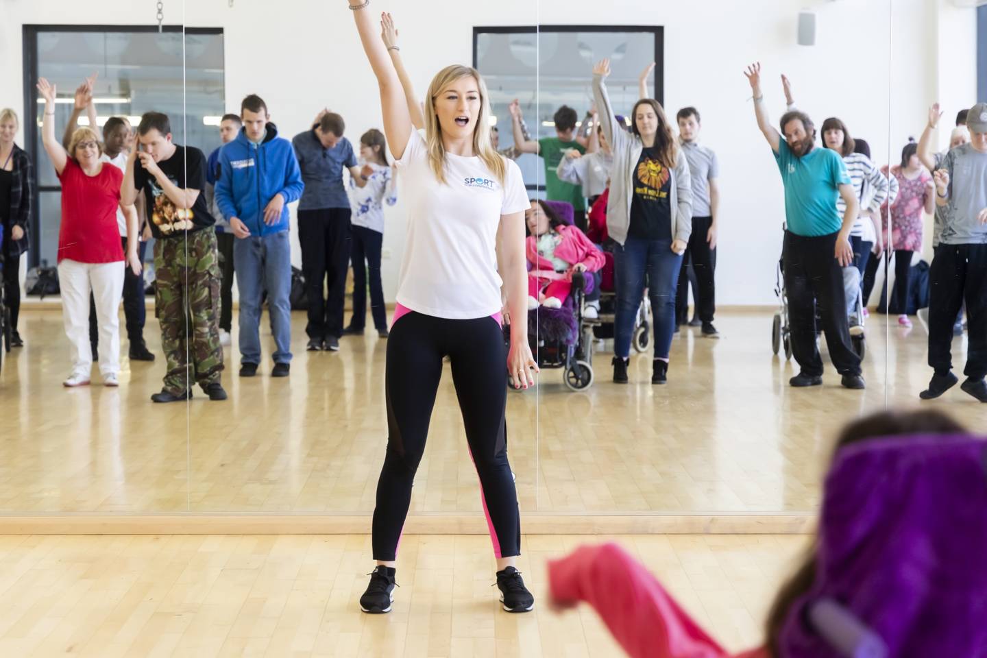 Coach delivering activity session to group of disabled and non-disabled people in dance studio