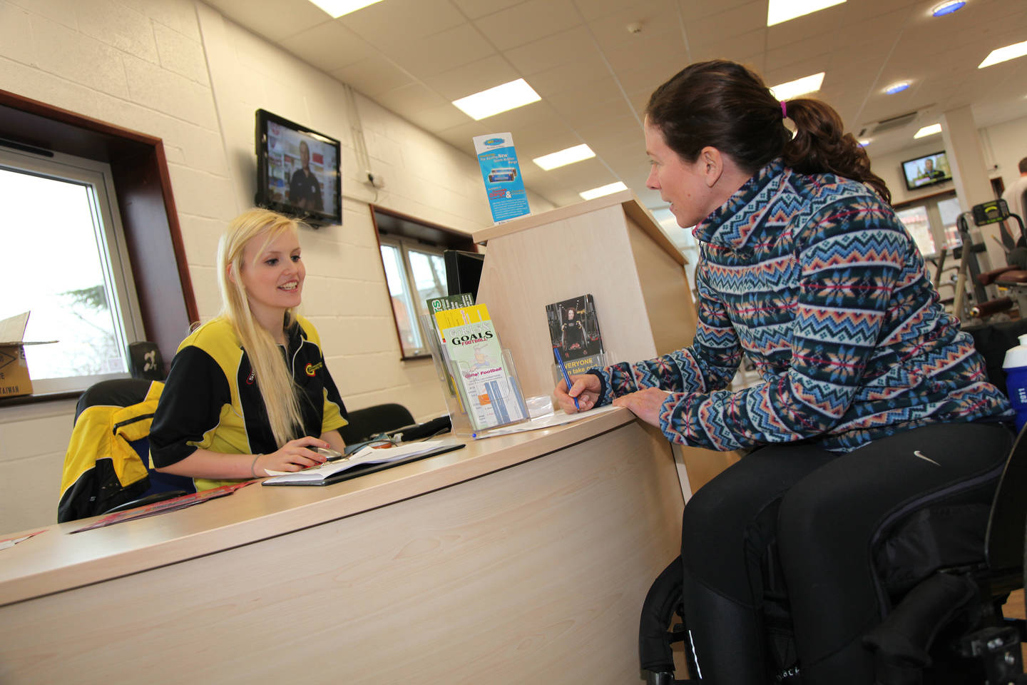 Female wheelchair user receiving great customer service from receptionist at leisure centre