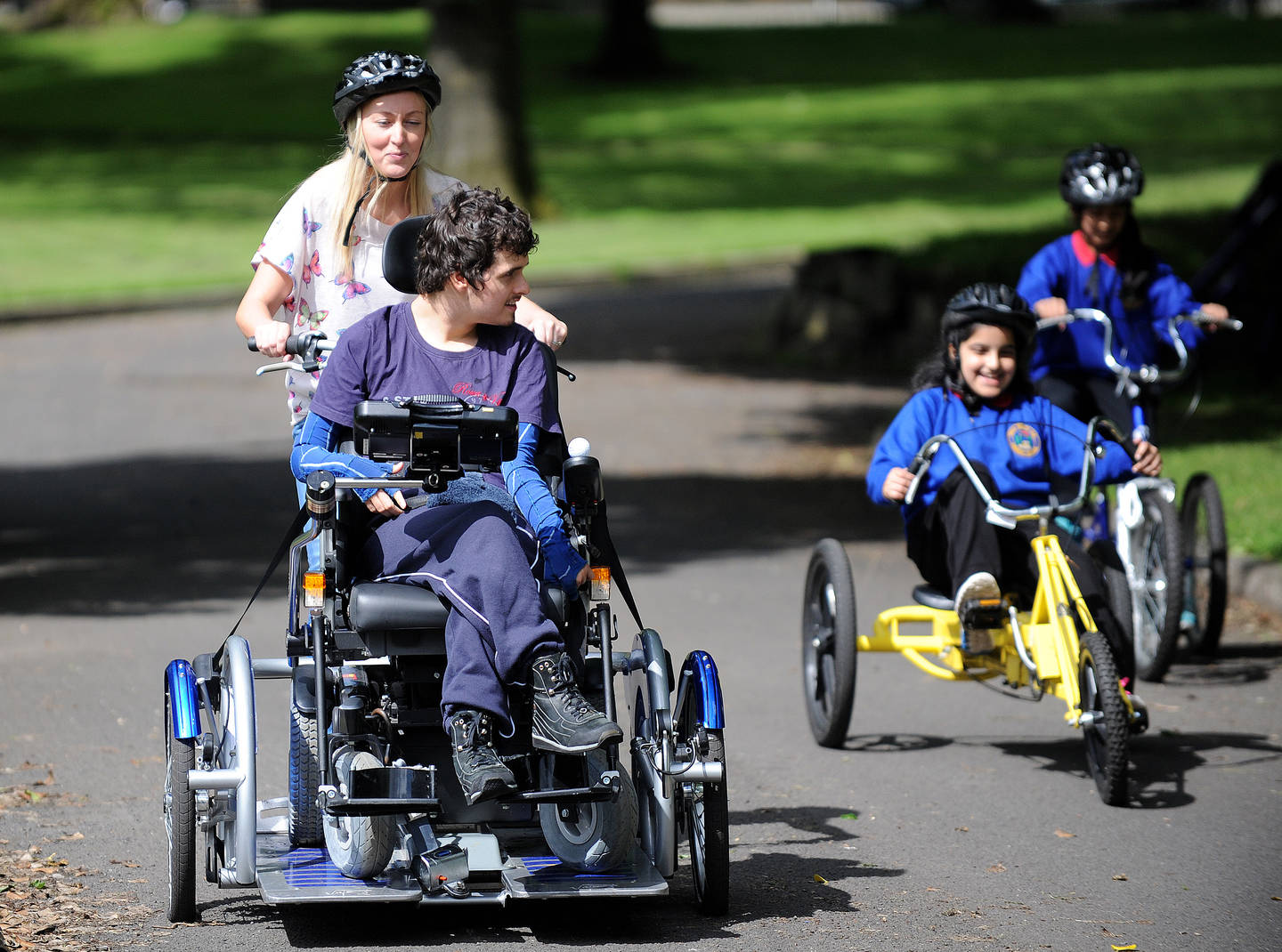 Young man riding adapted bike with supporter during a cycling session in the park  