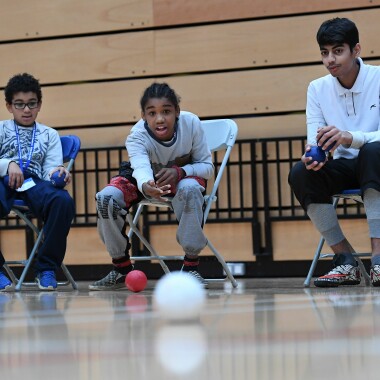 Three boys sitting down playing a game of boccia