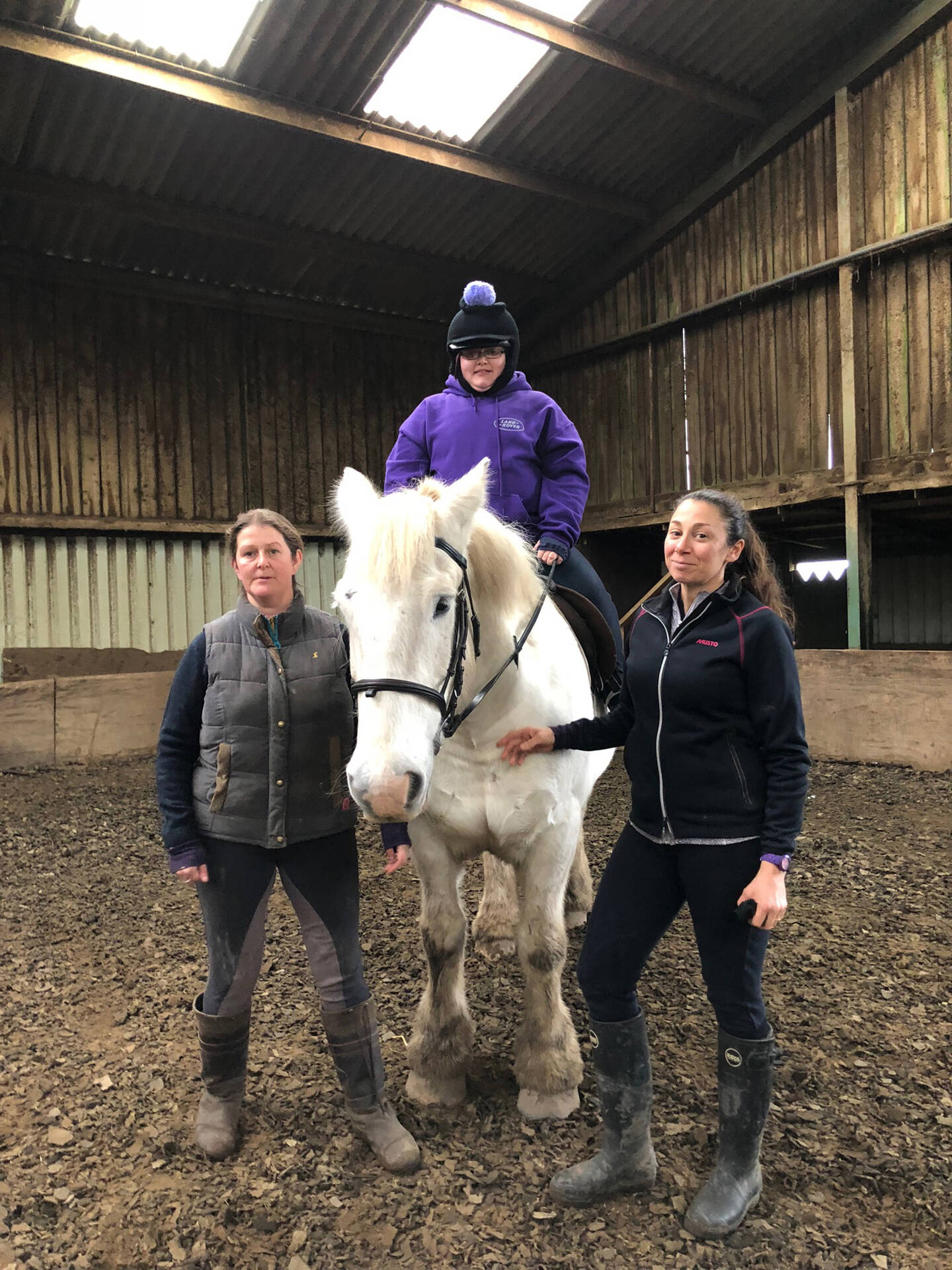 Disabled rider on white horse supported by two RDA volunteers. 