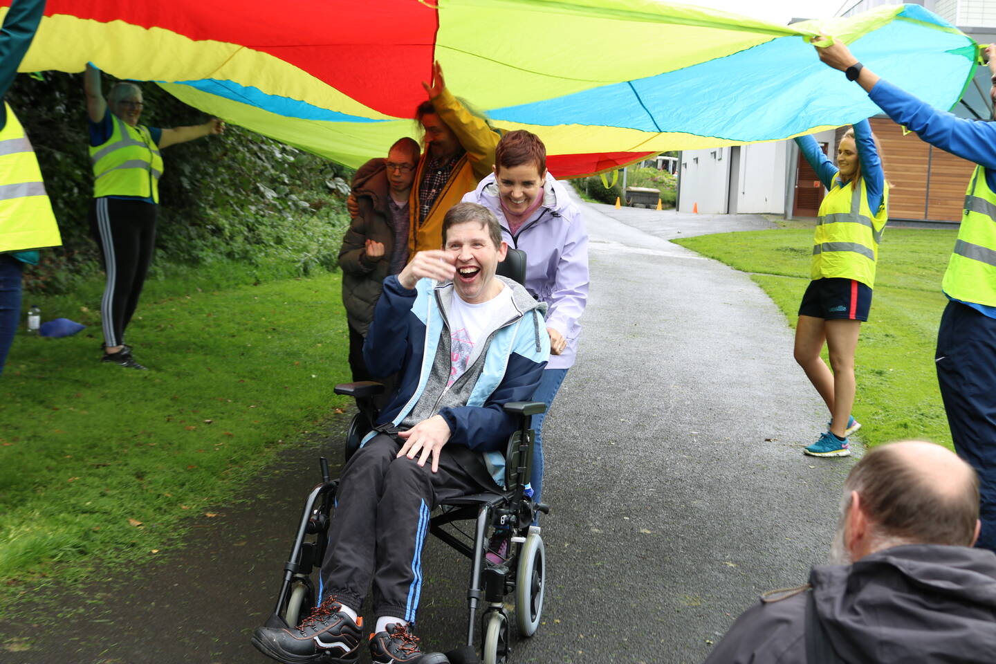 Wheelchair user smiling and laughing while going under a colourful parachute held up by volunteers 