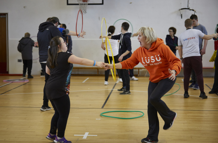 A teacher and a disabled child play with a hula hoop in a school sports hall