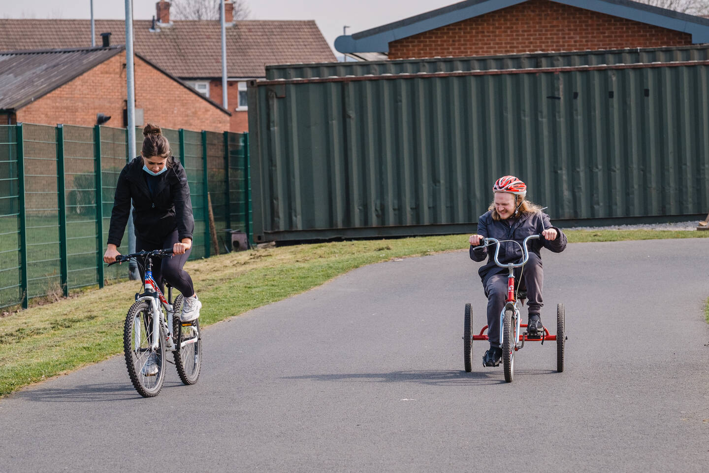 Young disabled man riding an adapted bike around a park with his supporter 