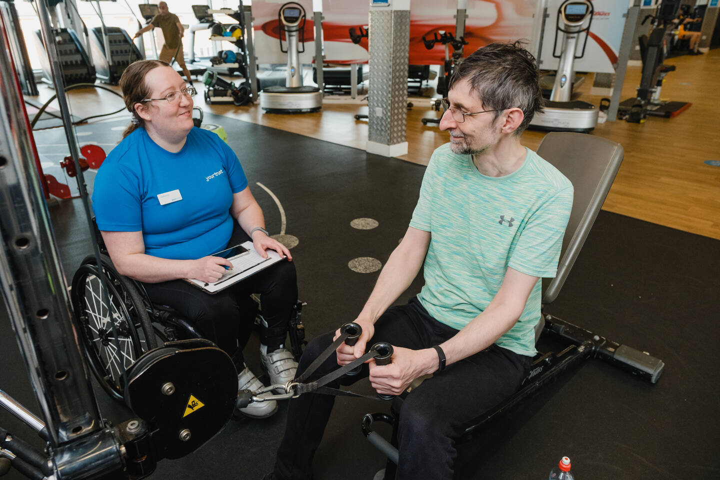 Catherine, a disabled personal trainer supporting client in the gym