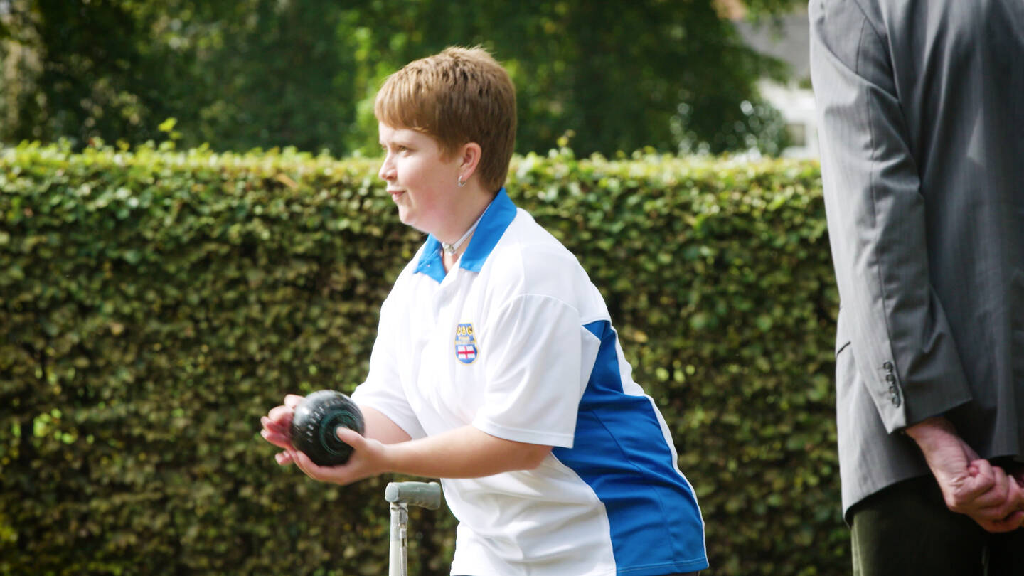 Woman with visual impairment playing bowls outside on bowling green