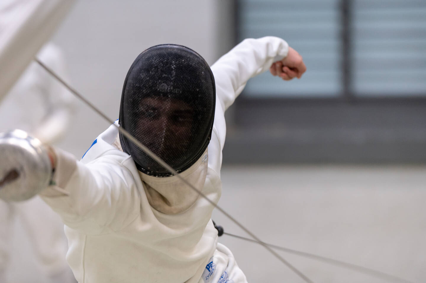 A fencer in a white top with black face shield lunges forwards.