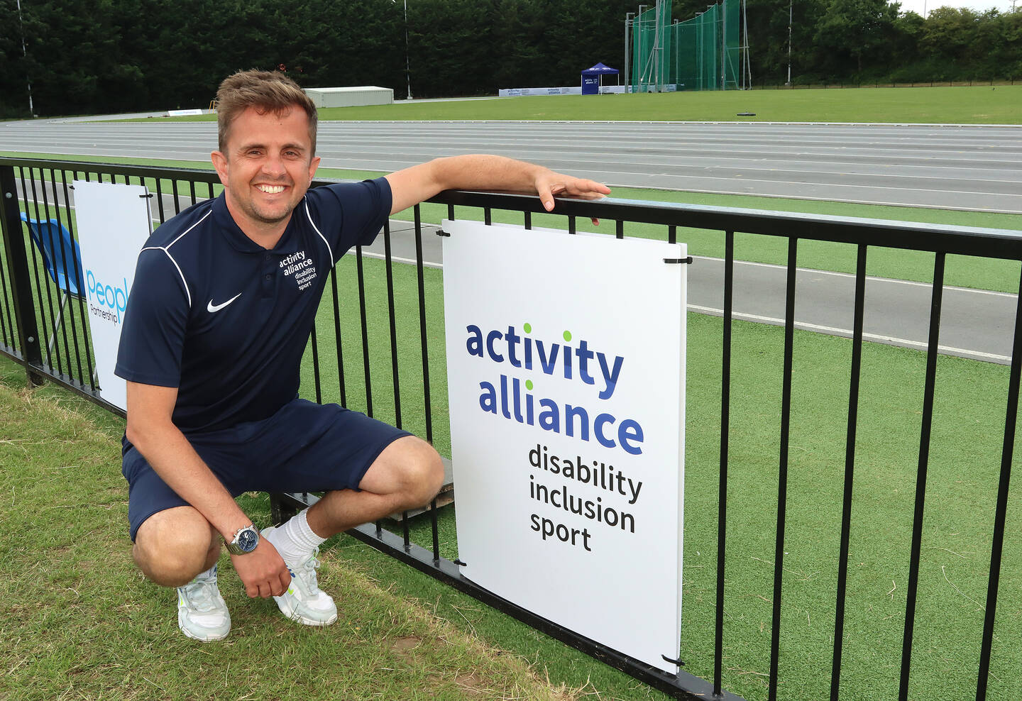 Adam Blaze, CEO of Activity Alliance, crouches next to the Activity Alliance logo on a board.