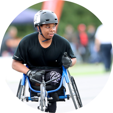A junior wheelchair athlete wearing a helmet and racing gloves getting ready to race on an athletics track.