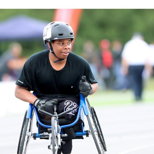 A junior wheelchair athlete wearing a helmet and racing gloves getting ready to race on an athletics track.