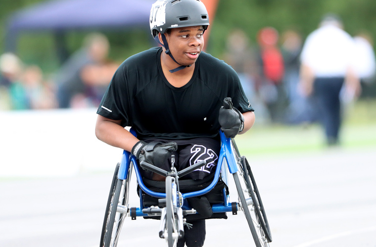 A junior wheelchair athlete wearing a helmet and racing gloves getting ready to race on an athletics track.