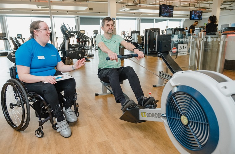 Disabled fitness instructor supporting her client to use the rowing machine in the gym