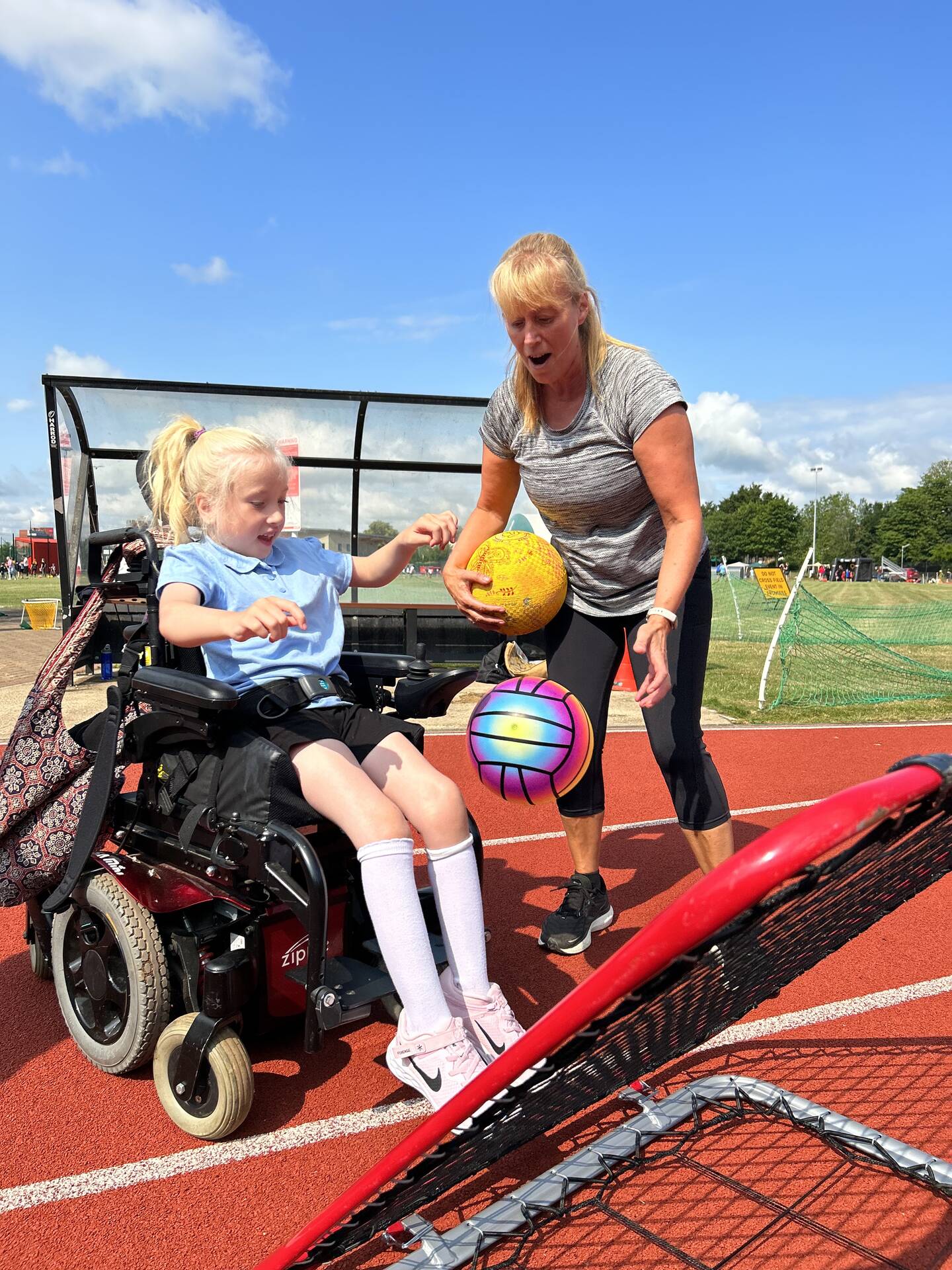 Disabled girl and woman playing with a net and a sports ball on an athletics track. 