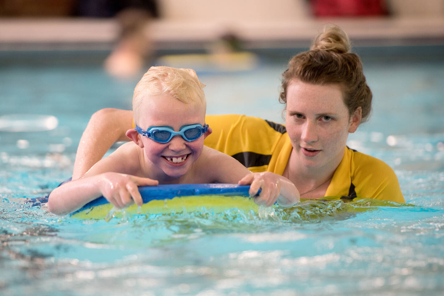 Young boy with visual impairment having fun swimming on a float with support from his swimming teacher.