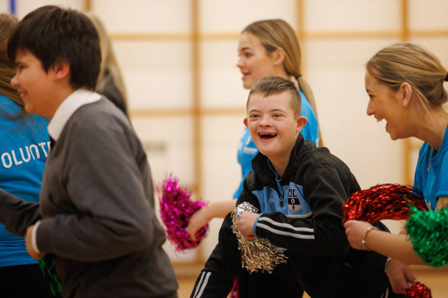 Group of disabled and non-disabled people taking part in a dance using pom poms in a sports hall.
